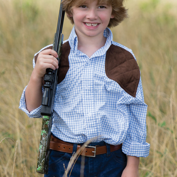 Young boy wearing a blue tattersall performance shooting shirt with brown quilted shoulder patches in a field.