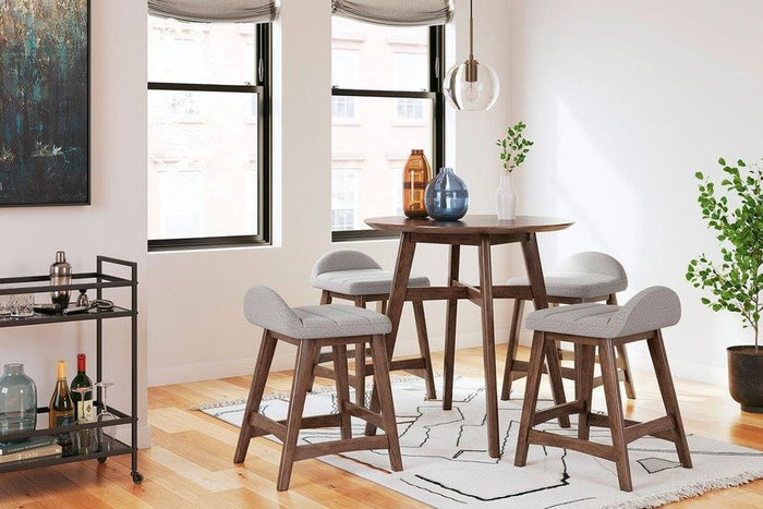 Full lifestyle view of light gray upholstered bar stools around a round bar table in a bright, modern setting.