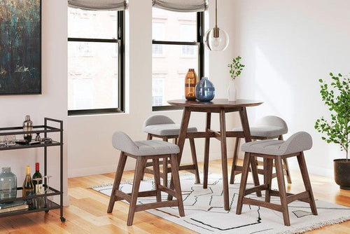 Full lifestyle view of light gray upholstered bar stools around a round bar table in a bright, modern setting.