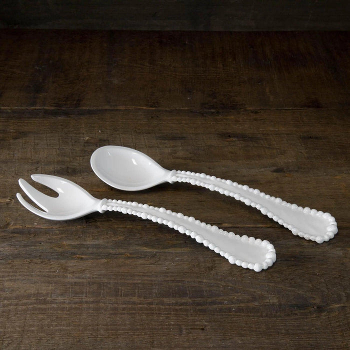 White melamine salad servers with pearl-rimmed handles on a rustic wooden surface.