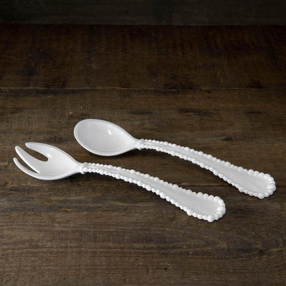 White melamine salad servers with pearl-rimmed handles on a rustic wooden surface.