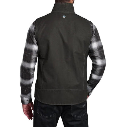 Back view of a dark olive Kuhl cotton canvas vest layered over a grey and black plaid flannel shirt.