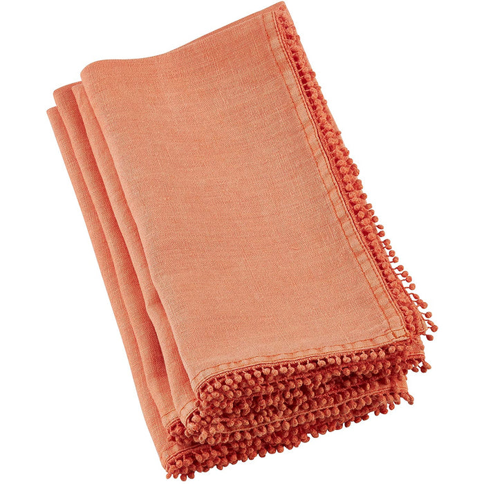 Folded coral-colored linen and cotton blend napkin with decorative pompom trim edges on a white background.