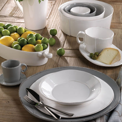 Vietri Lastra white pasta bowl with rustic textured edges, set on a grey dinner plate on a wooden table.